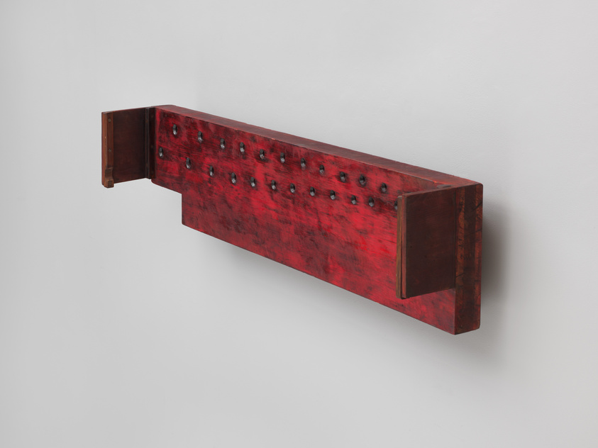 A red, textured shelf with rivets, mounted on a white wall.