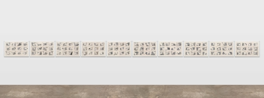 A long row of framed black and white photographs displayed on a white gallery wall, each frame containing multiple images.