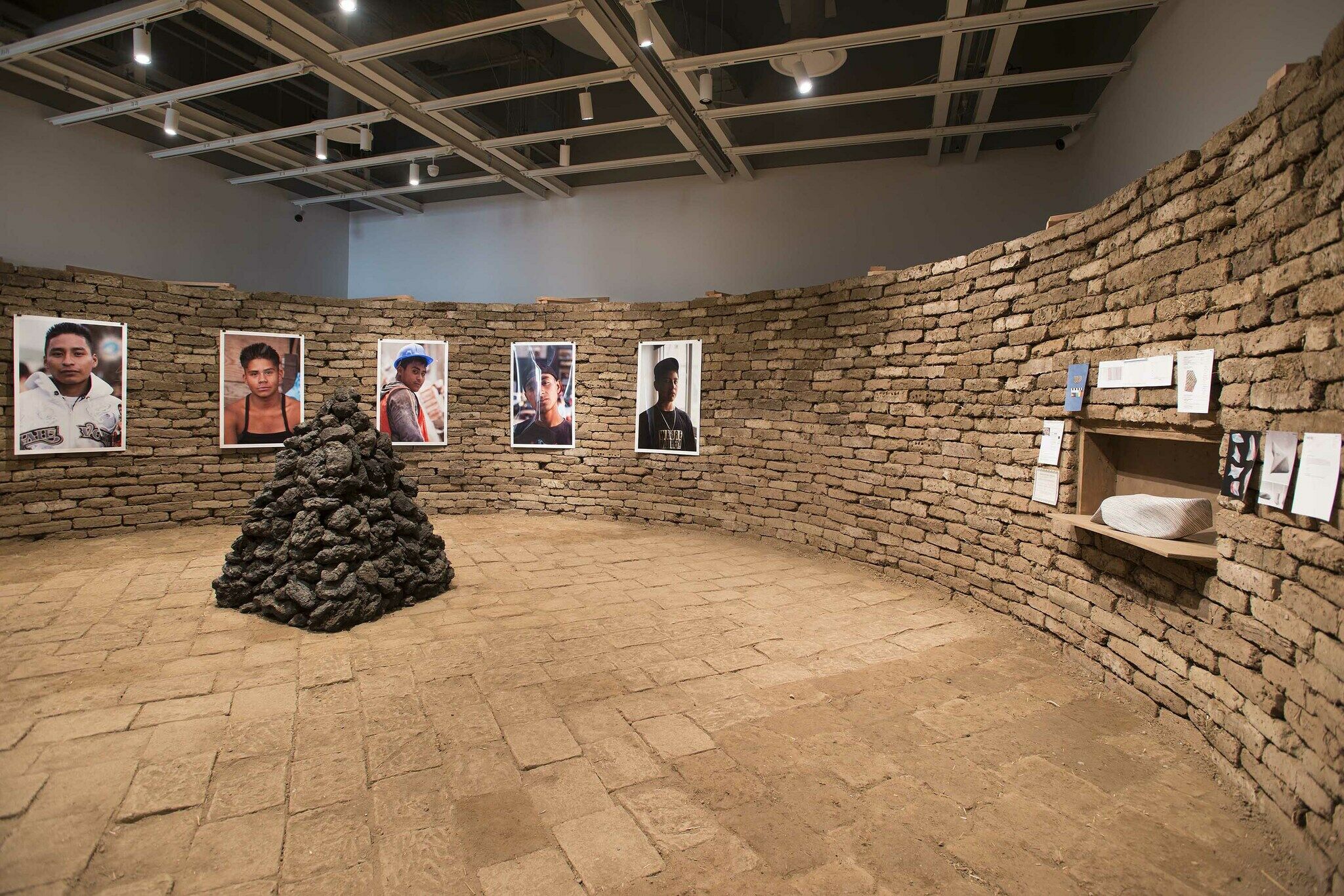 An installation view of a brick wall displaying works of art.