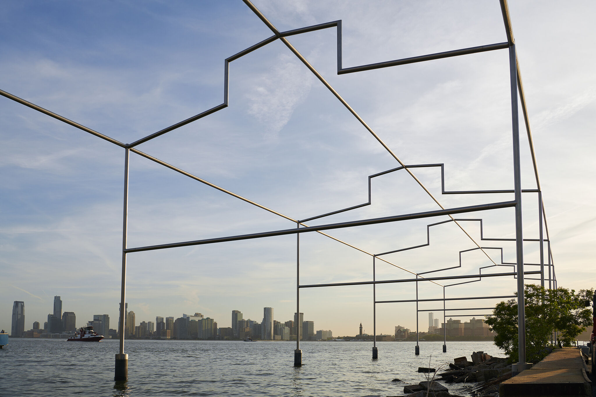 Close-up frontal view of Day's End steel sculpture from underneath, with New Jersey skyline in the background.