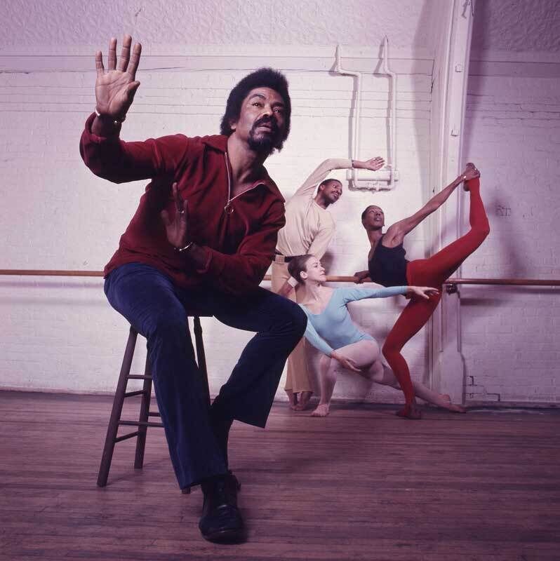 A photograph of Alvin Ailey seated in the foreground, with a trio of dancers in the background.