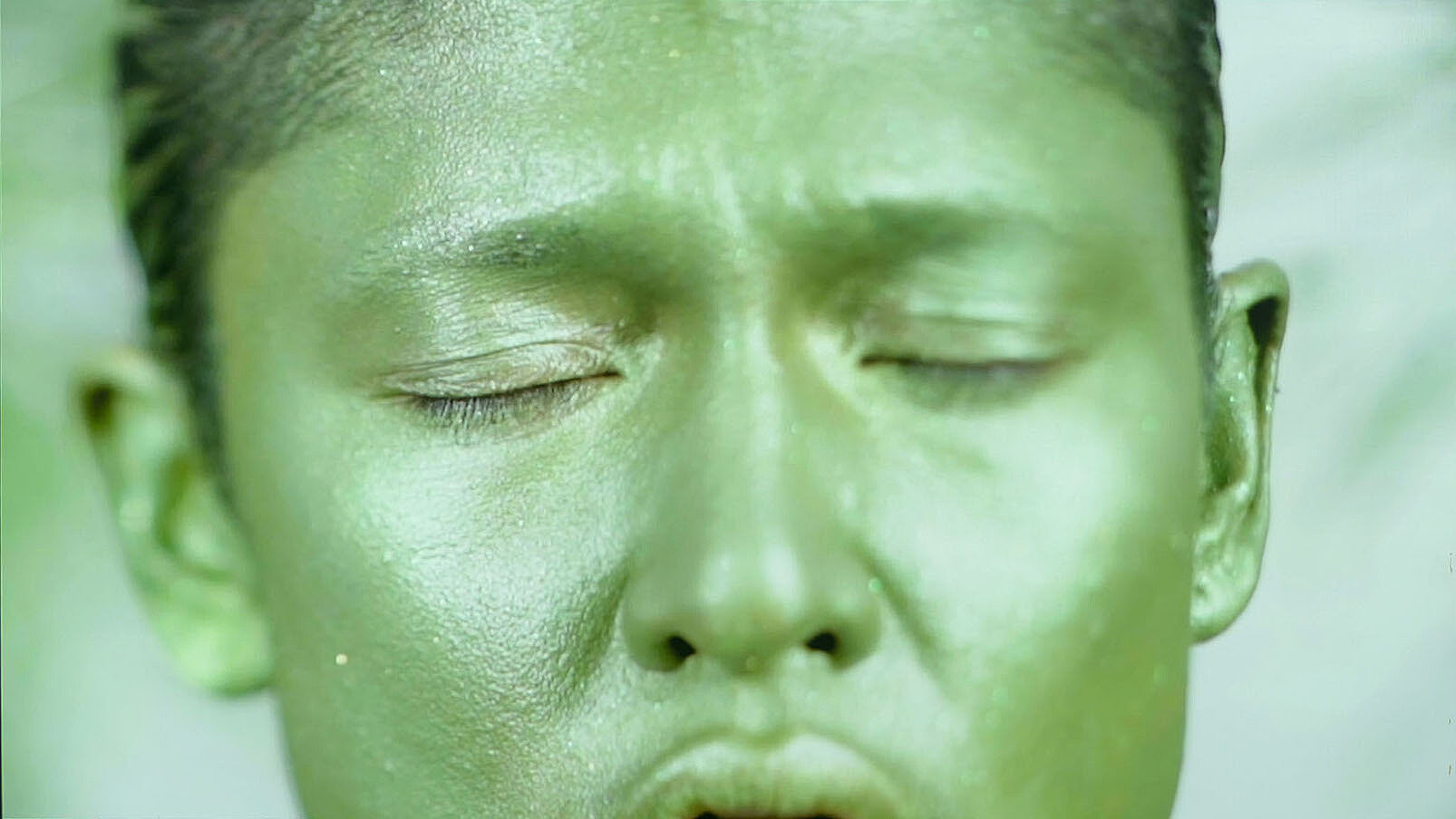 A close up video still of a person's face painted green.