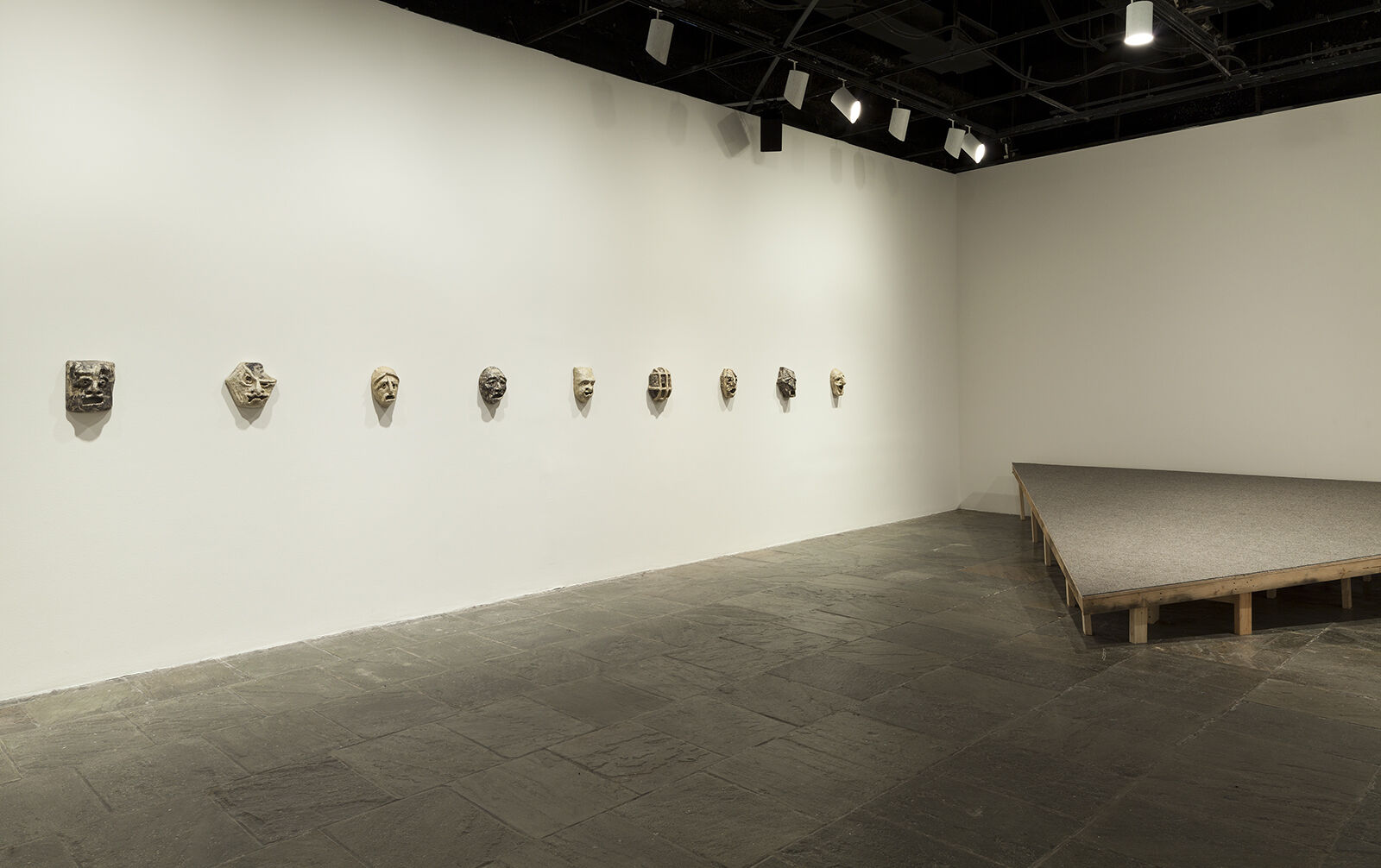 A gallery with masks displayed in a line across a wall.