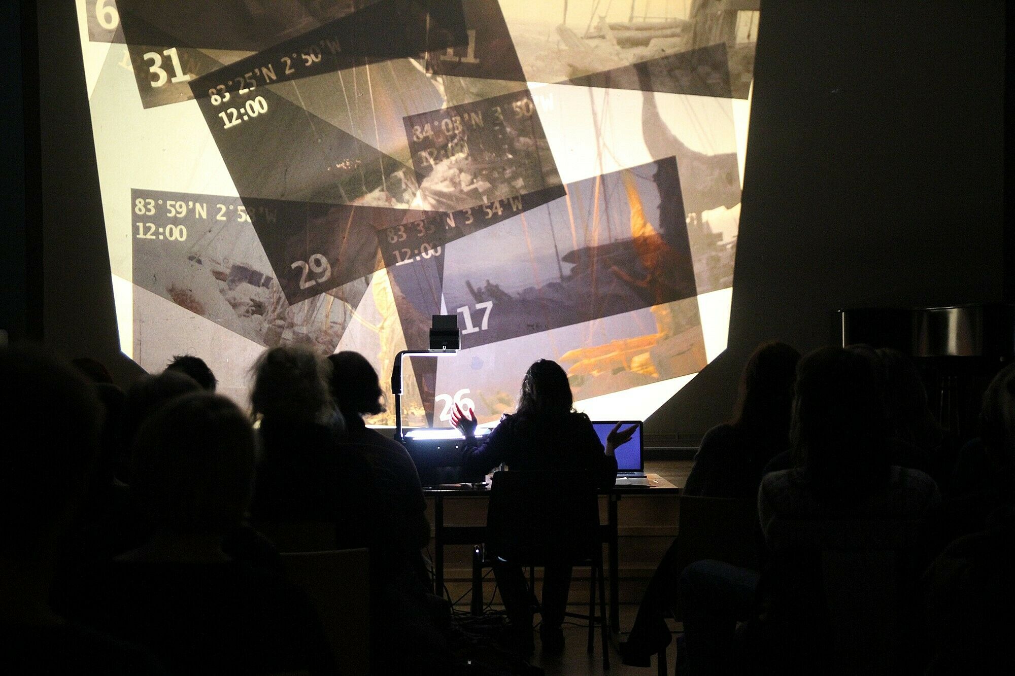 A performance view of a person sitting in front of a wall with projected images.