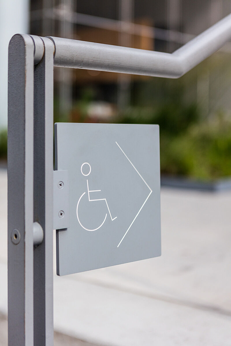 A sign displays a wheelchair icon and an arrow attached to an outdoor bannister.