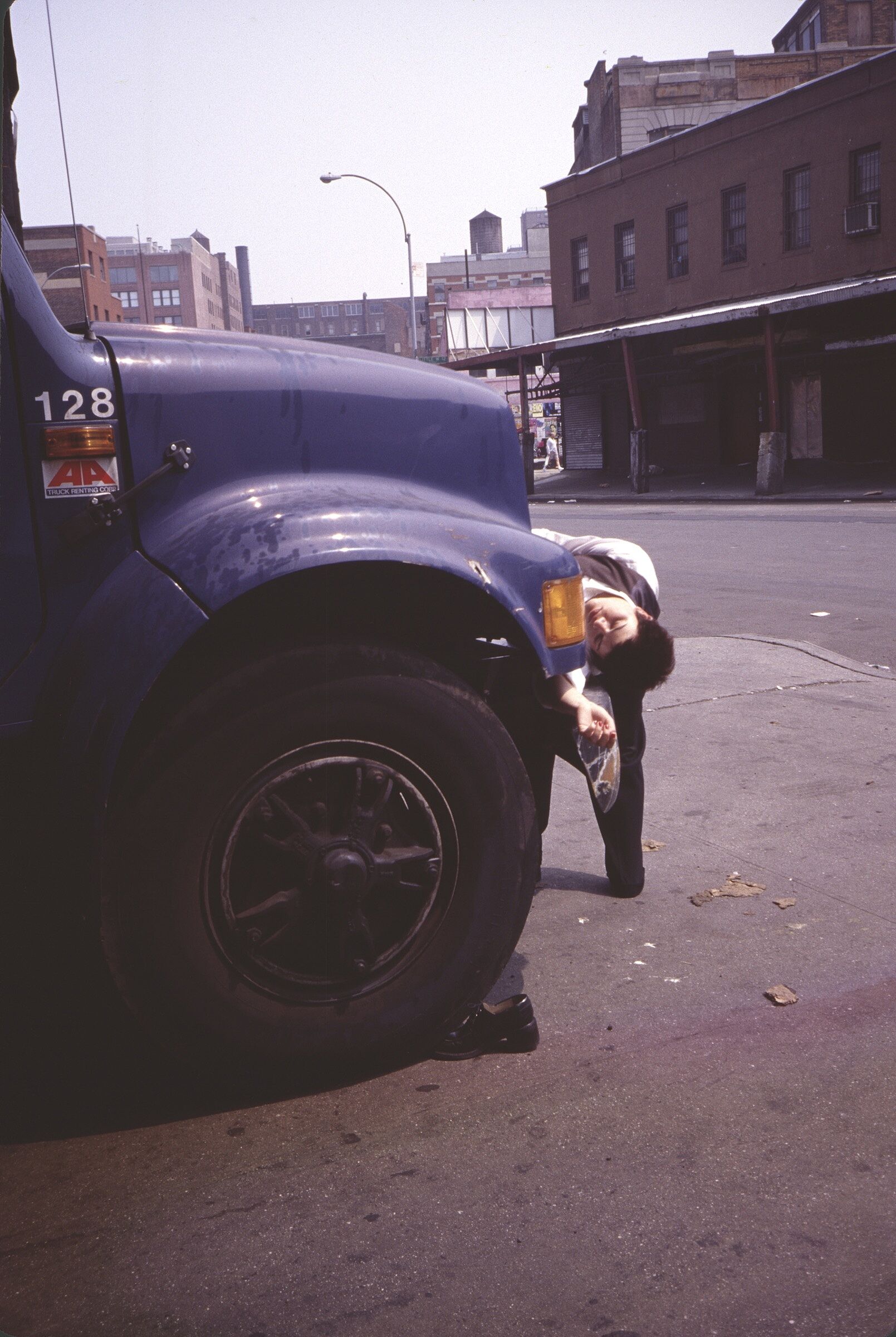 A film still of a person bending backward behind a blue truck.