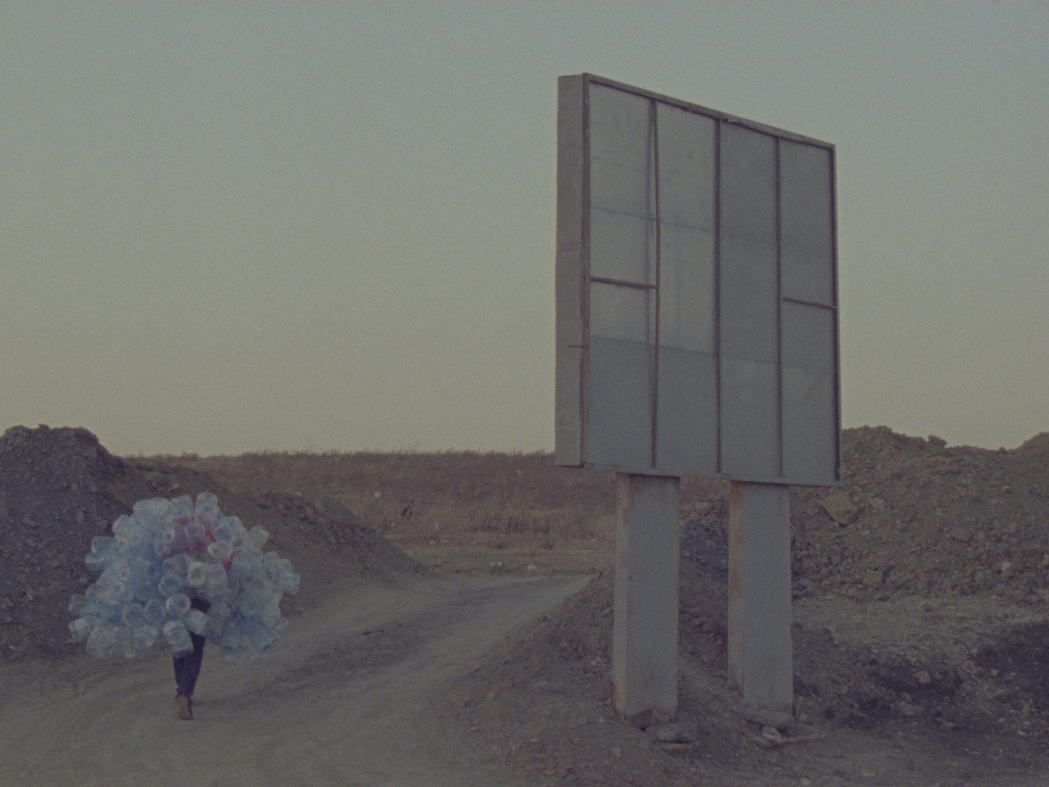 A person walks down a dusty road holding a large number of plastic bottles. 