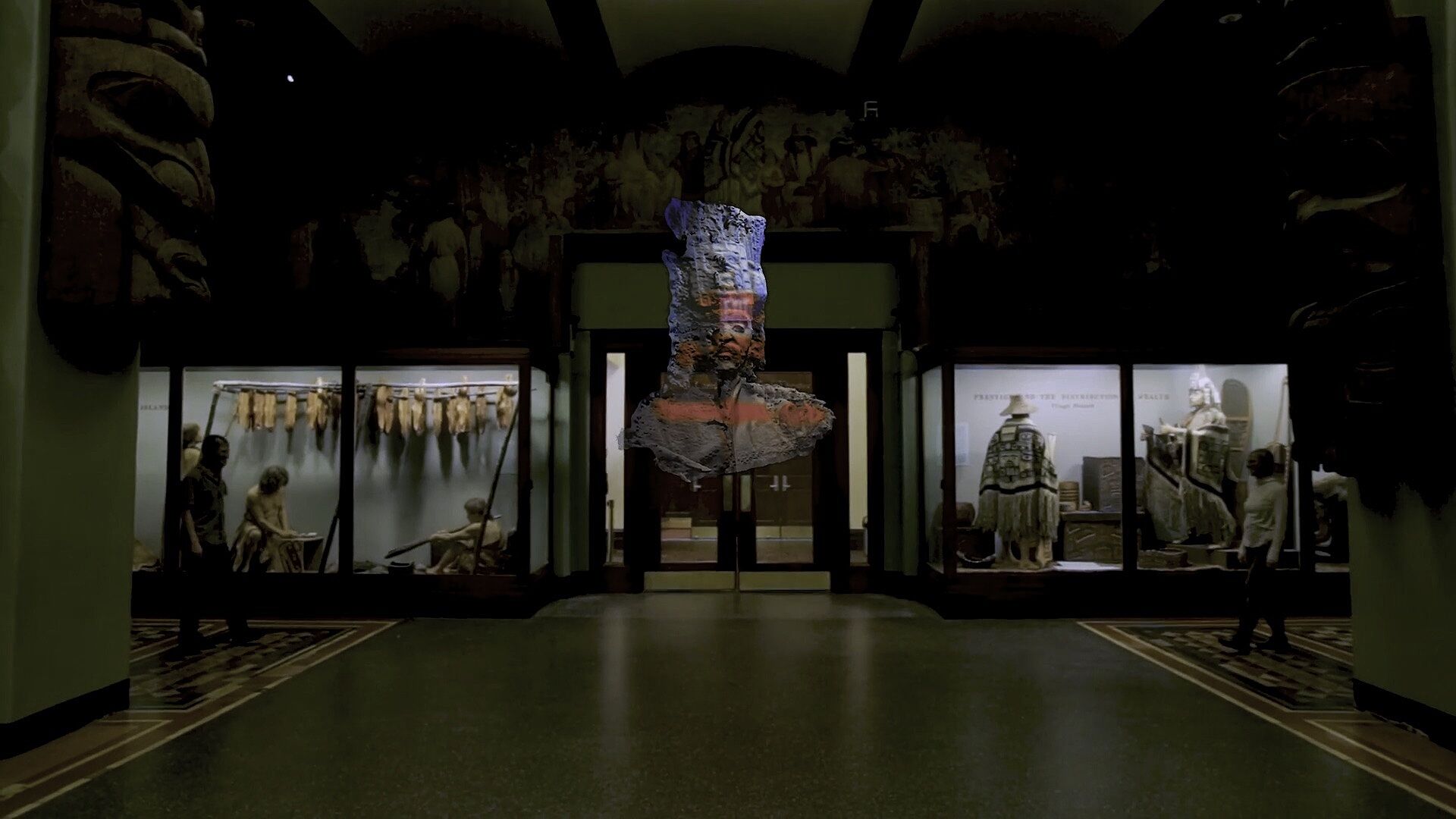 A view of an installation of a sculpture in the center of a room with other glass encasements of cultural objects.