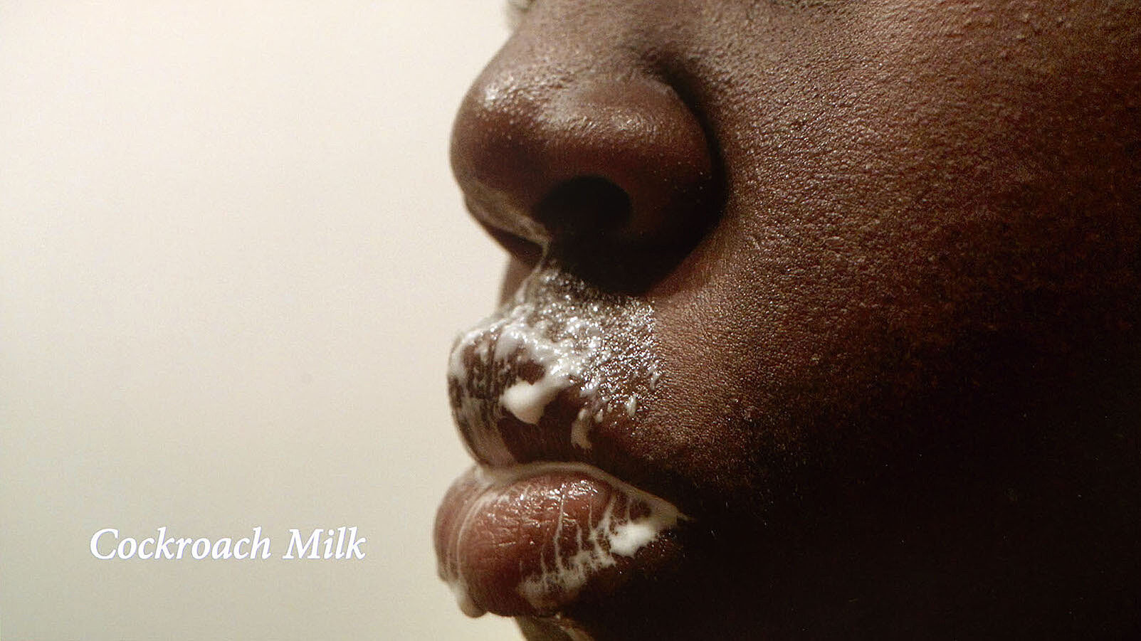 A close up video still of a person's face cover in white liquid.