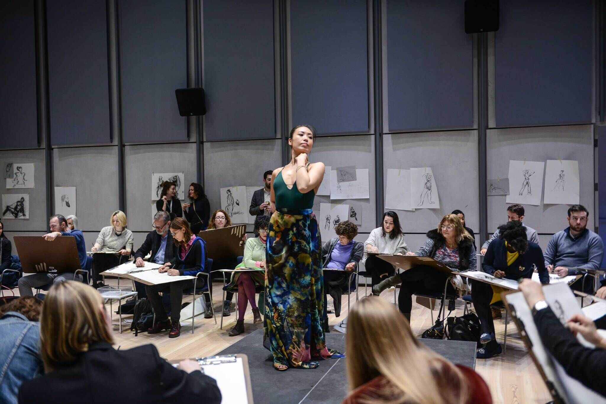 A performer in the middle of the room with people at desks all around them watching.