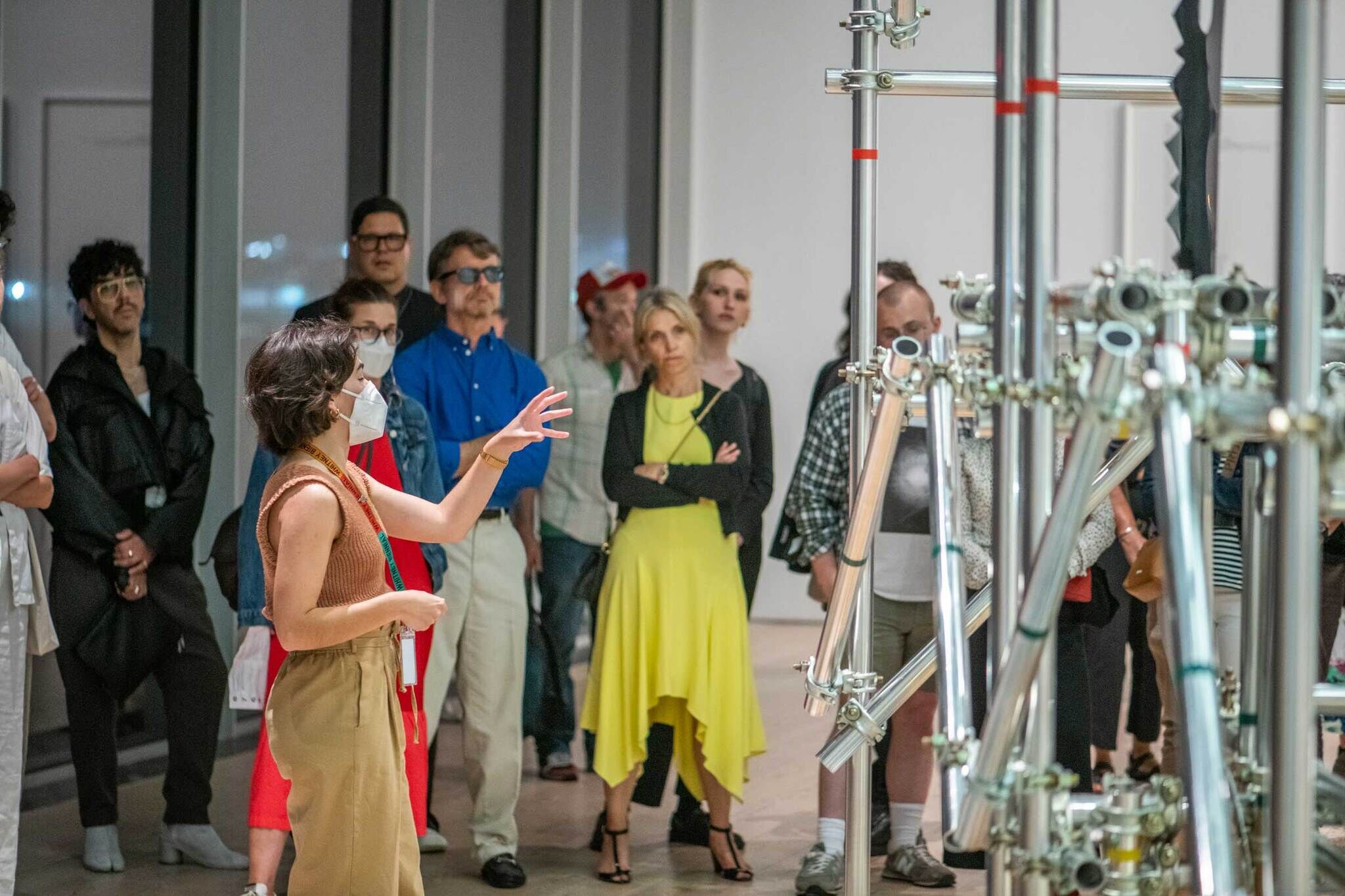 A docent in a mask giving a tour to many people in the background.