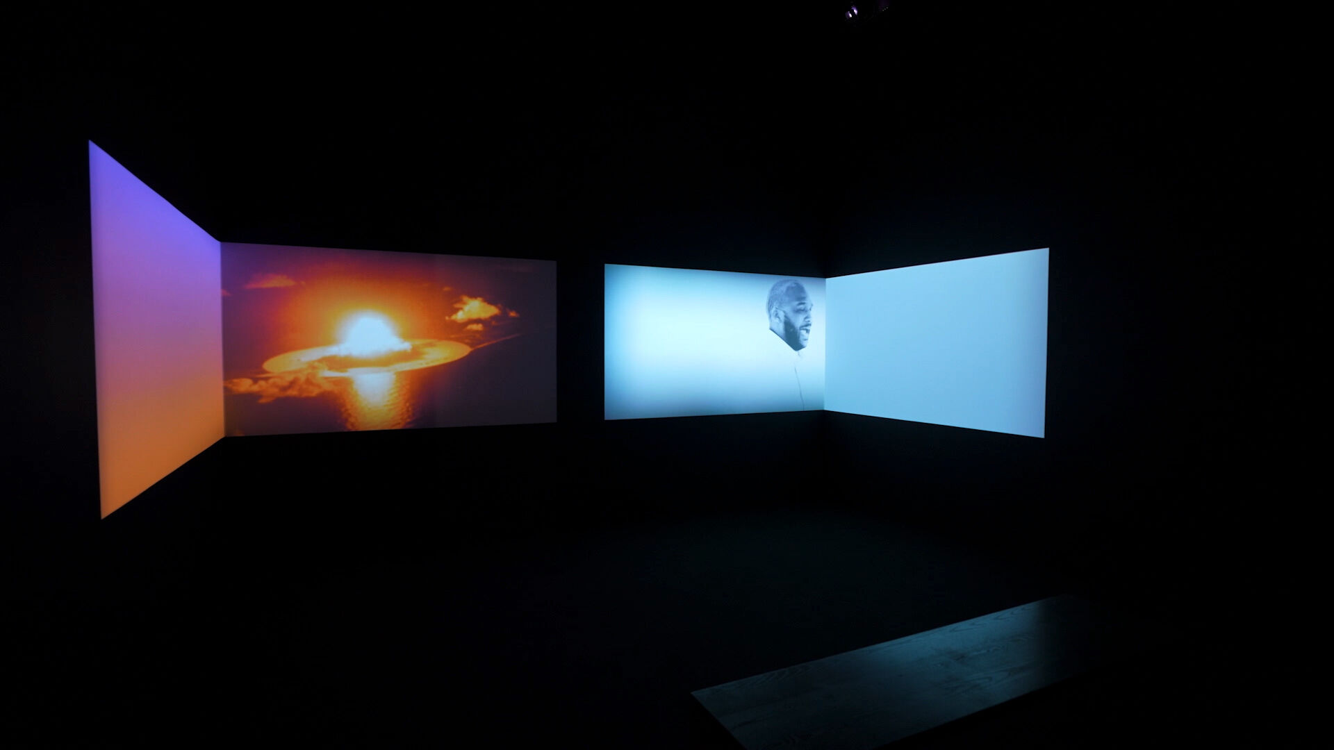 Four projection screens of orange and blue tones in a blackened room.