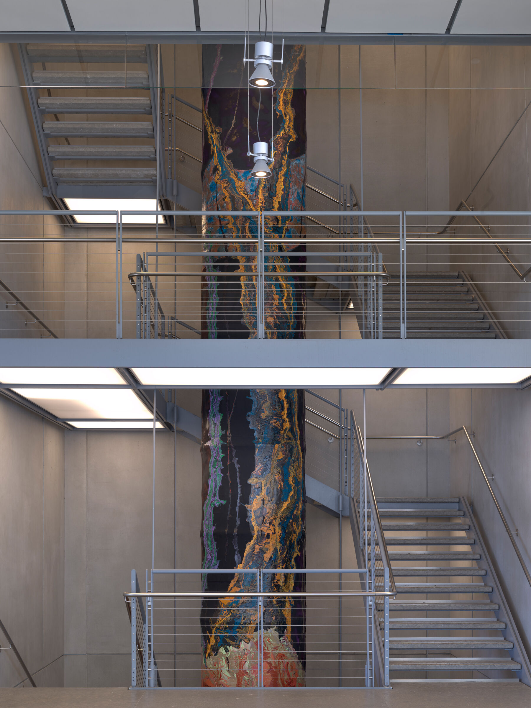 Colorfully painted cylinder running through the shaft of a stairwell 