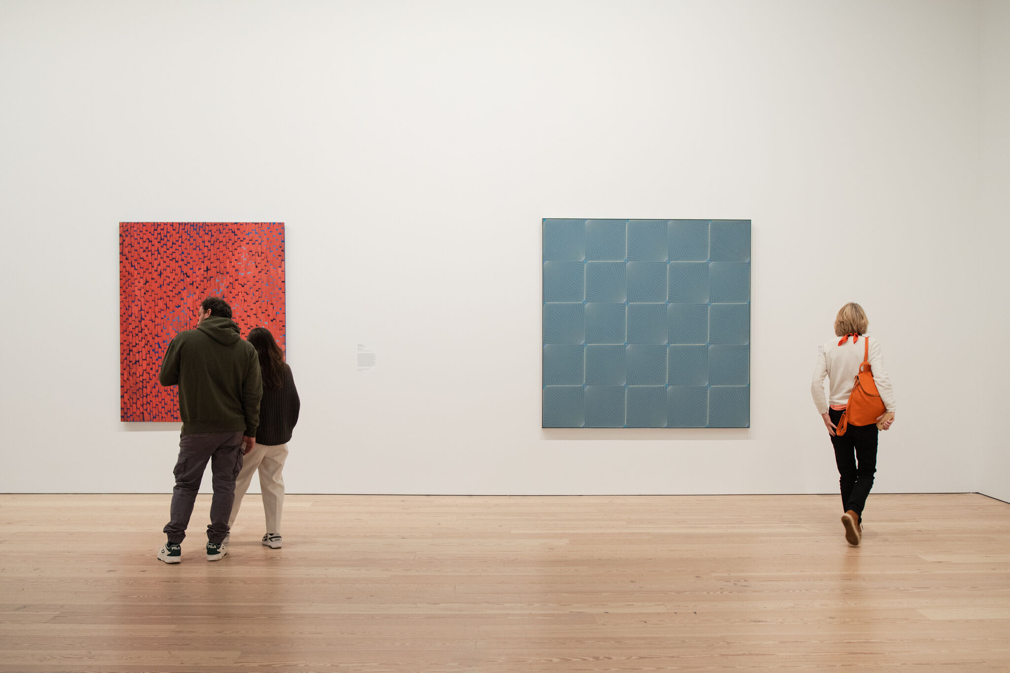 People stand in galleries in front of two large and bright paintings. 