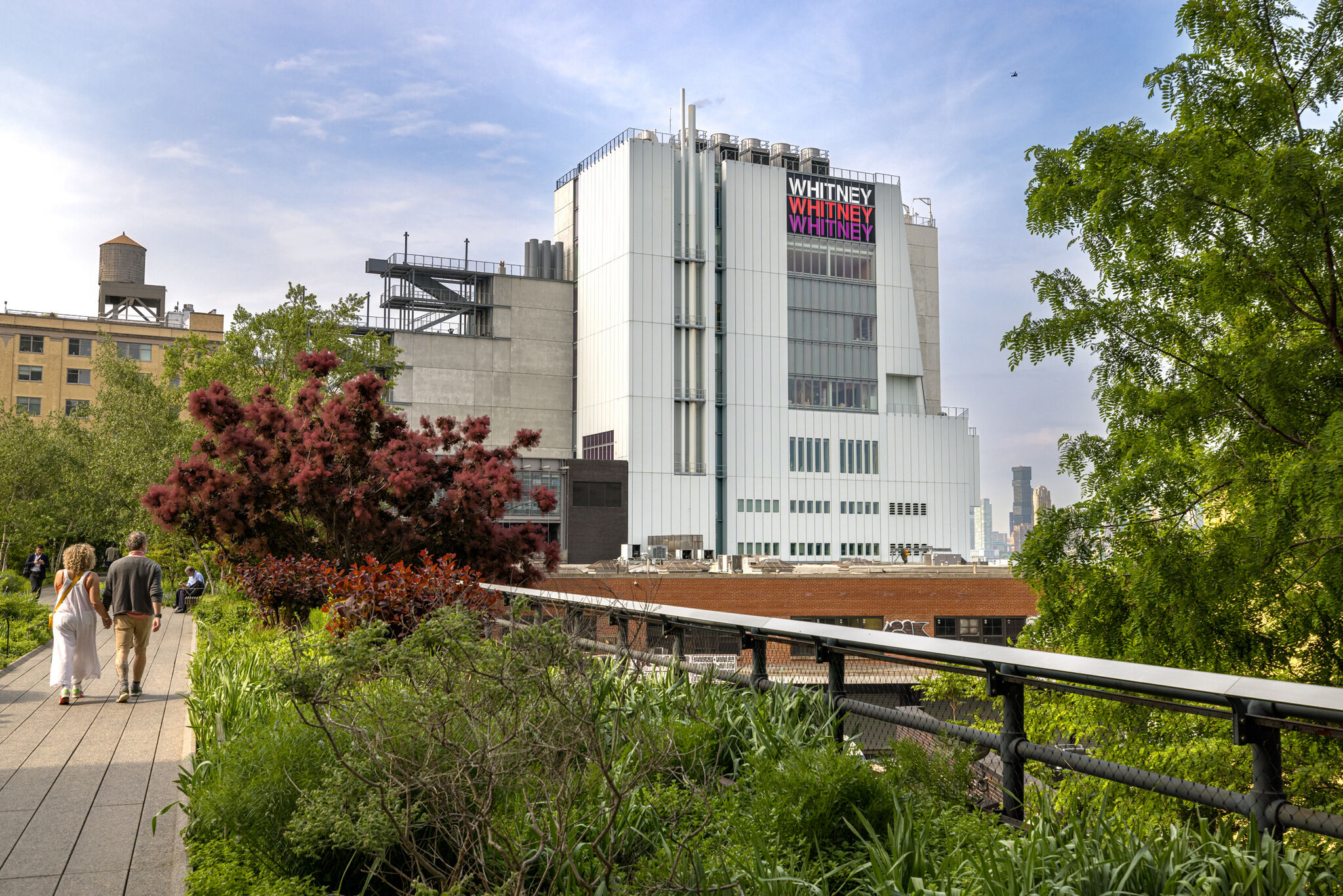 Two people walk down the High Line with a view of the Whitney Museum behind. 