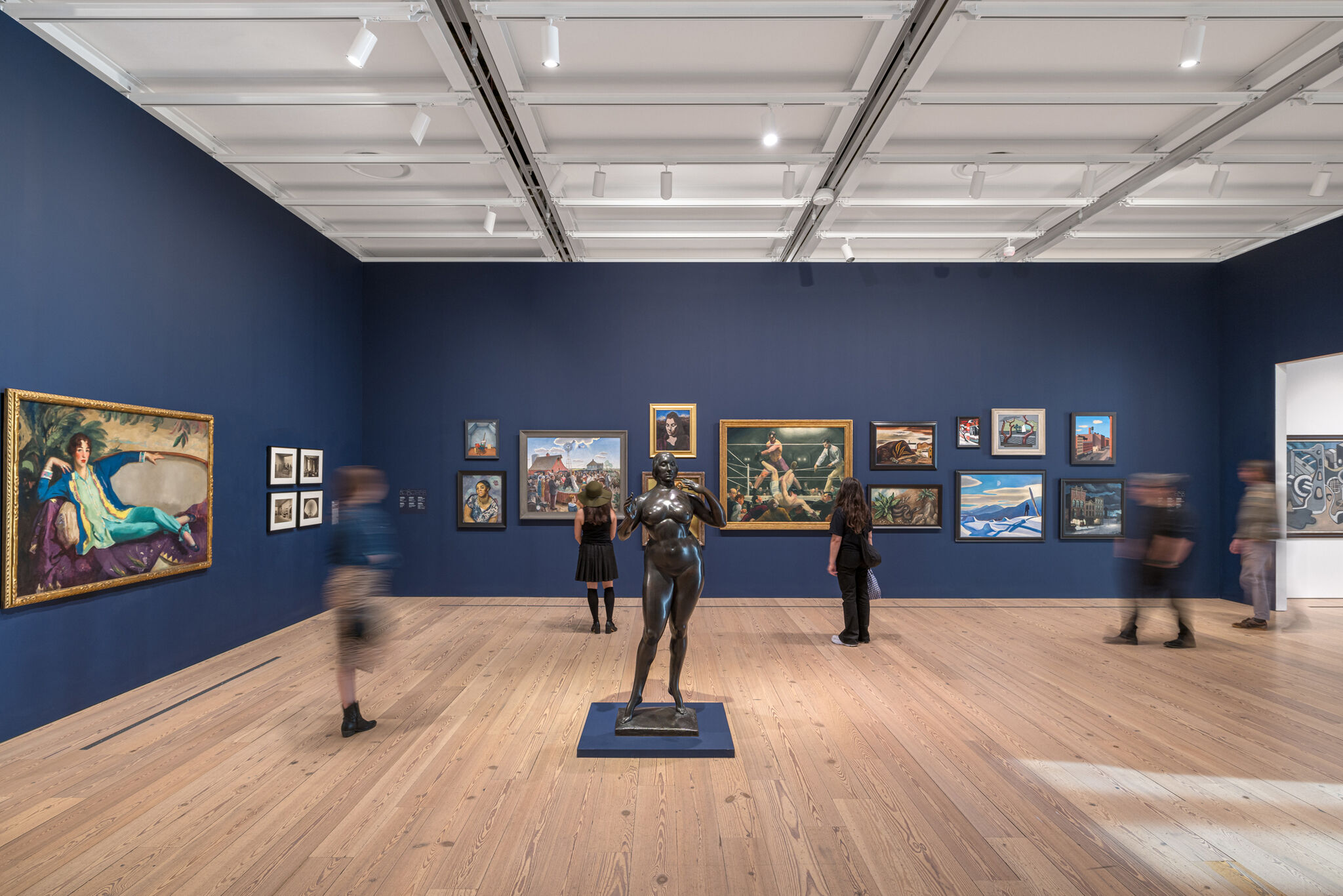 Two people look at a wall covered in paintings.