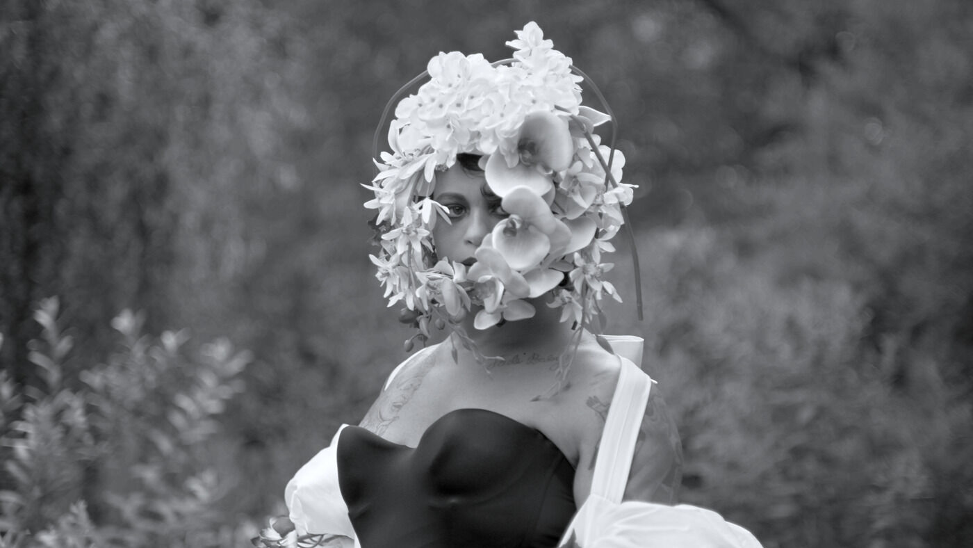 Woman adorned with a floral headpiece in a black and white photo.