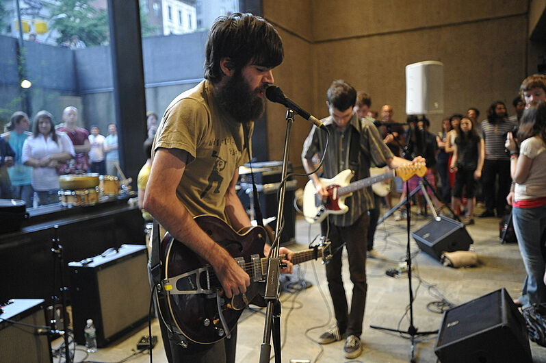 A bearded man sings while playing guitar in a lower floor of the museum.