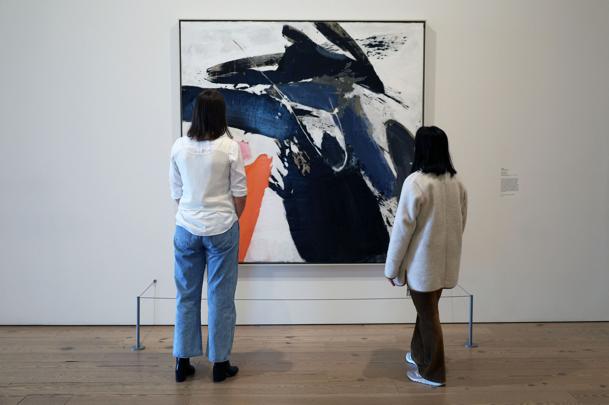 People standing in front of a large painting with wide swaths of color pulled across a white background. 