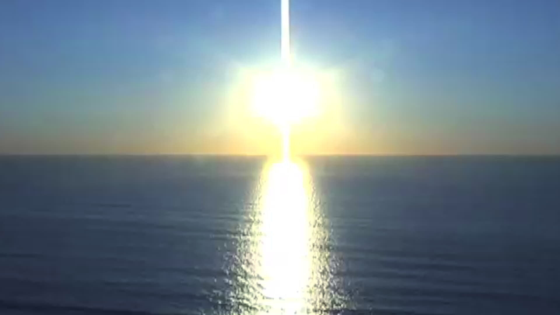 A screen displays a vibrant sunset over the ocean, with the sun's reflection creating a bright vertical line on the water.