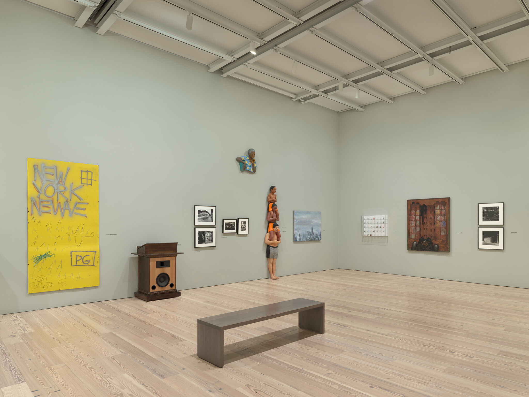 Art gallery with various paintings and sculptures on display, including a yellow "New York New Wave" piece and a stacked figure sculpture.